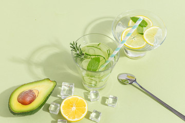A glass beaker, of cucumber water, fruits and cutlery on a light green background. Minimalistic creative concept. Copy space.