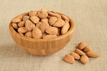 Big shelled roasted salted almonds in bamboo bowl on rough linen cloth