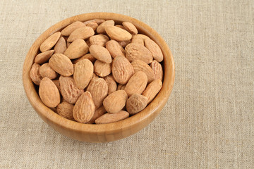 Big shelled roasted salted almonds in bamboo bowl on rough linen cloth