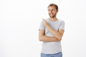 Fototapeta premium Dreamy and creative ambitious male entrepreneur standing over white background pointing and gazing at upper left corner with pleased happy smile feeling delight and satisfaction enjoying nice view