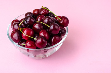 Glass bowl with cherry on pink background