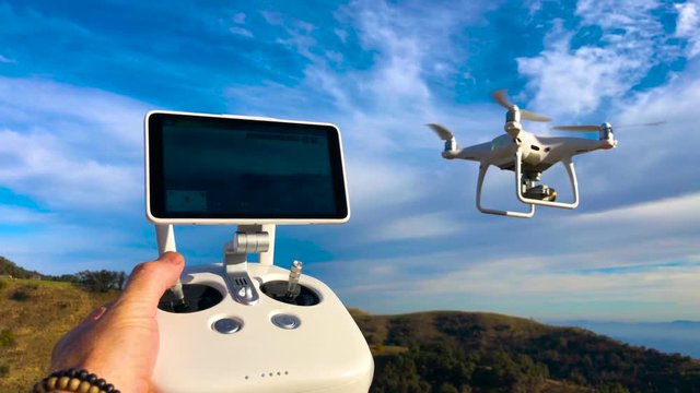 Drone Flying abobe the mountain tops blue sky green grass sun set Ojai phantom .  Drone flying quadcopter  with white RC transmitter. Controlling drone over RC radio controller. Man flying and filming