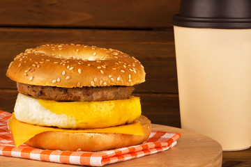 Sandwich breakfast with wooden plank in background. Bagel, egg, cheese, and sausage.