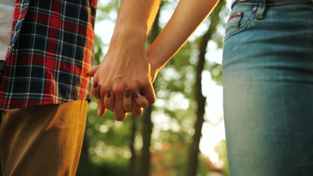 Close up of a male hand taking and holding female hand. Green park on the background. Couple of husband and wife . Outdoors