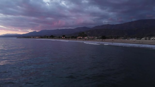 Sunset Drone Towards Beach Over Waves With Homes Mountains and Vibrant Sky