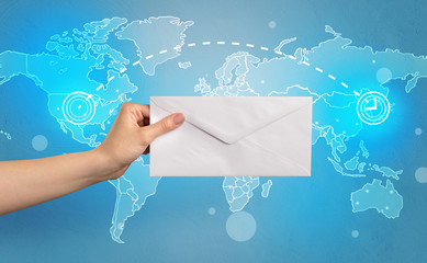 Female hand holding coloured and white envelope with blue map on the background
