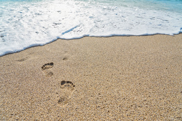 Footprints and a white foam on a sandy beach. Copy space.