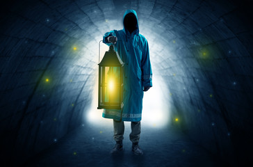 Ugly man in raincoat walking with glowing lantern in a dark tunnel