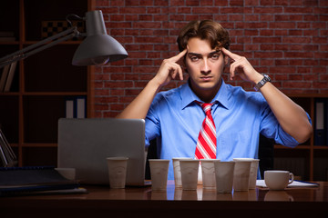 Young employee drinking coffee working at night shift 