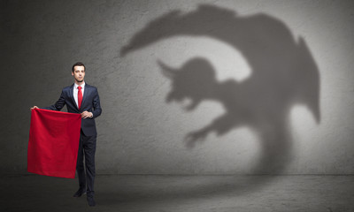 Businessman standing with red cloth in his hand and imp shadow on the background
