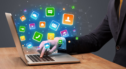 Businessman hand typing on laptop with flying application icons around

