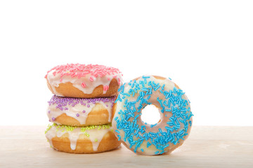Vanilla cake donuts frosted and covered in candy sprinkles on a light wood table isolated on white. Tasty homemade delight