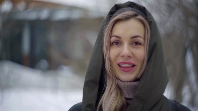 adult blonde woman with dark eyes and braces on teeth is smiling broadly outdoors in winter day