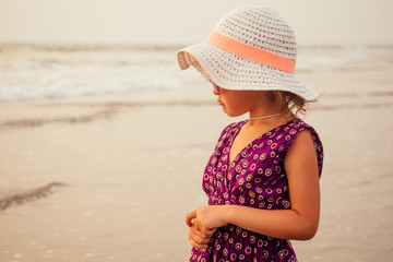 Pretty little baby girl in a violet dress and hat and sun glasses relaxing on the beach near sea, summer, vacation, travel concept. smiling cute little girl on beach vacation spf and sunscreen