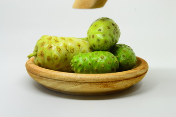 Noni fruit on top of a wooden bowl with a white background