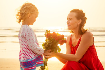 little girl blonde gives a bouquet of roses to mother on the beach.beautiful mother and daughter...