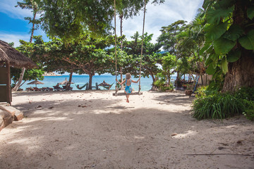 Vacation young woman in blue swimsuit swinging at palm grove enjoying sea view on Koh Tao, Thailand