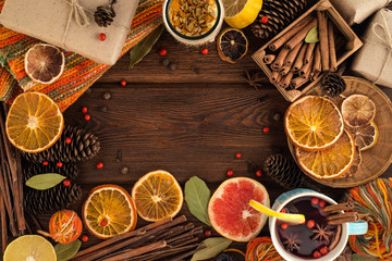 Cosy still life with bakery set: mulled wine, cinnamon, anise, lemon and dried citrus. Christmas bakery concept background. Mulled cider in blue ceramic glass, knitted warm textile and given boxes.