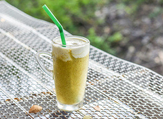Glass of healthy cold drinks kiwi smoothie with cream on steel grating bar.