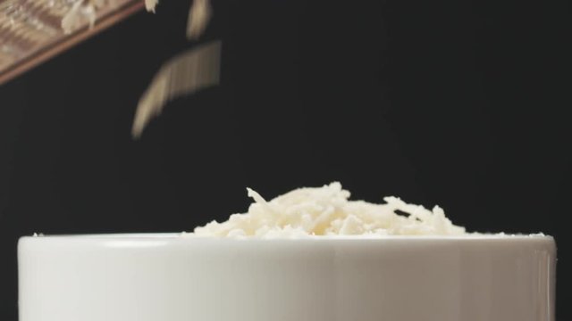 Slow motion closeup of grating aged parmesan in white bowl on wood table