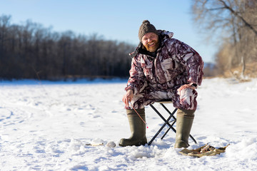 Bearded european man is smiling while he fishing on the river at winter day time