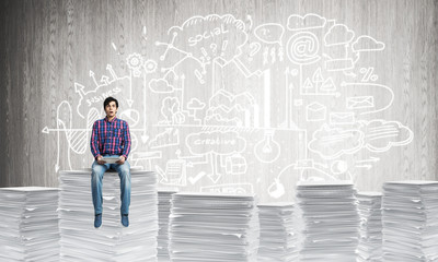 Attractive man sitting on pile of paper documents.