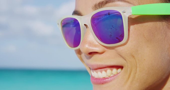 Woman smiling on summer beach wearing sunglasses. Face closeup of funky happy girl having fun in summertime.