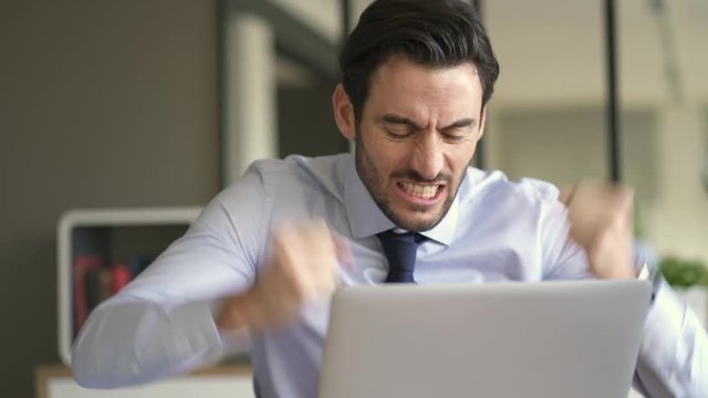 Angry businessman losing patience and screaming at laptop in modern office