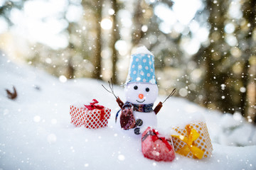 Happy snowman with gift boxes standing in winter christmas landscape. Snowman smiling standing in snow near spruce trees