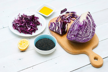 red cabbage salad ingredients with unpeeled sesame seeds and olive oil on white wood table