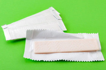 Chewing gum and bubblegum concept theme with closeup on an unwrapped stick of peppermint gum and a bunch of sticks still in the wrapping foil in the background isolated on green