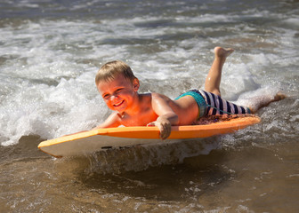 Young boy body boarding fearlessly in shallow waves.
