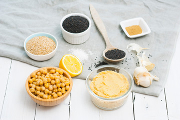 hummus spread and ingredients: chick pea, sesame seeds, garlic on creased canvas, white wood...