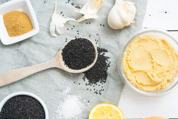 hummus spread and ingredients: chick pea, sesame seeds, garlic on creased canvas, white wood background