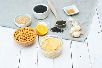 hummus spread and ingredients: chick pea, sesame seeds, garlic on creased canvas, white wood background