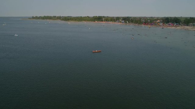 Aerial view of an old wooden boat in Lake Svityaz, a man rowing two oars, people swimming, beach, summer