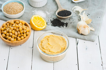 hummus spread and ingredients: chick pea, sesame seeds, garlic on creased canvas, white wood background