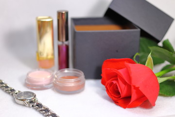 Obraz na płótnie Canvas アイシャドウとリップのコスメと赤い薔薇の花と女性用腕時計と空いたプレゼントの箱(白背景)