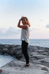 Teenage girl stands on rocky ocean coast