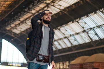 stylish bearded hipster tourist with backpack behind his shoulder on the platform of the railway station with a metal vault