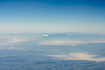 view from the window of the plane to the ground with mountains, rivers and horizon in the clouds and fog