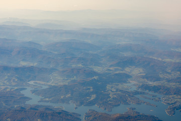 view from the window of the plane to the ground with mountains, rivers and horizon in the clouds and fog