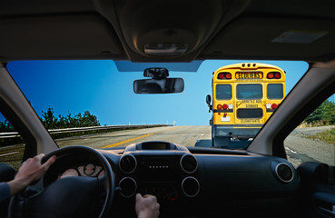 Young driver inside a car following a Yellow bus school