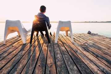 Men is relaxing and meditation on chair at footbridge on lake. Concept of waiting for summer.