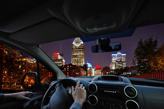 Young driver inside car on the road looking a night city landscape