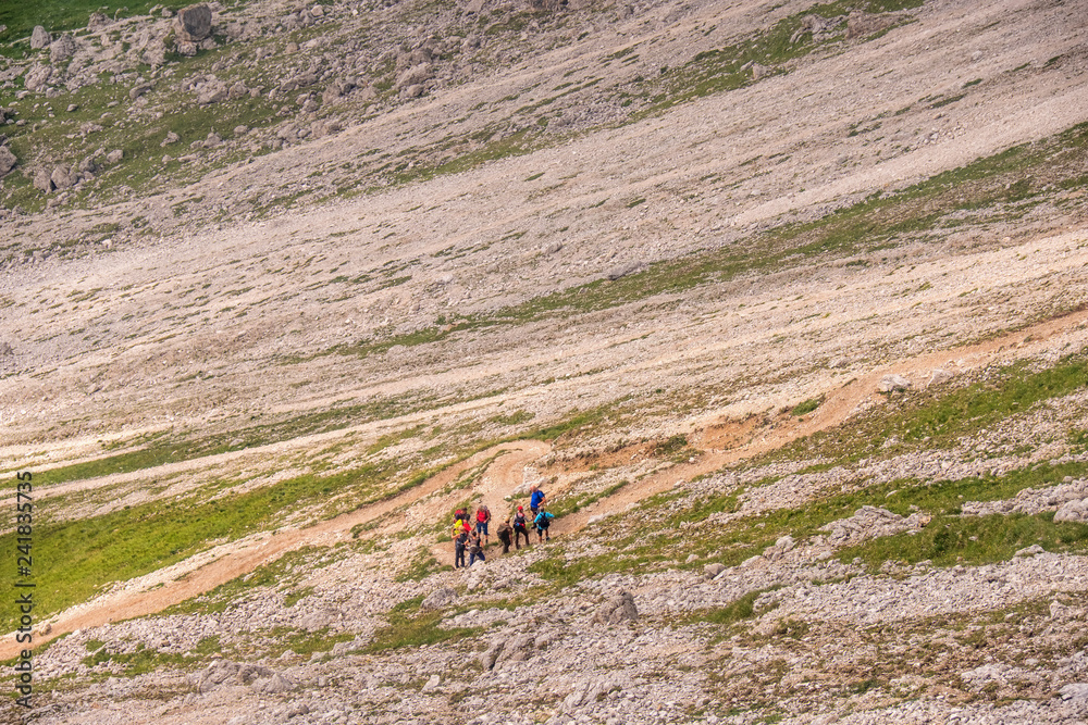 Wall mural Mountain Hikers on a winding road on a mountain slope