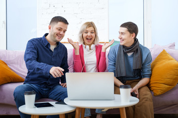 Friends sit on the couch, chatting and using a smartphone, desktop computer, laptop.