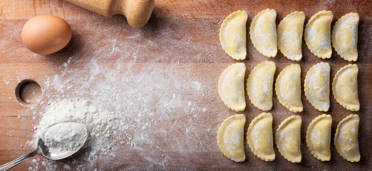 Raw panzerotti, homemade ravioli stuffed with ricotta and  spinach, with flour, egg and rolling pin on wood background. Top view, space for text