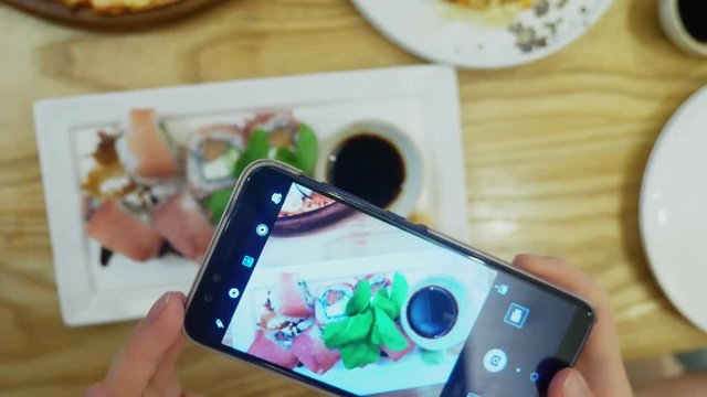 close-up. Female hands take a photo of sushi on a smartphone in a restaurant.