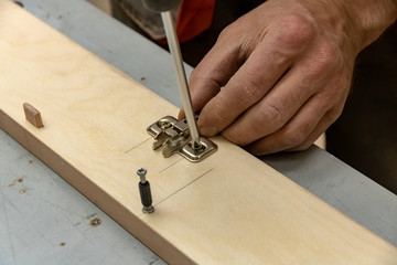 The furniture maker assembles the Cabinet, he tightens the screws with a screwdriver .